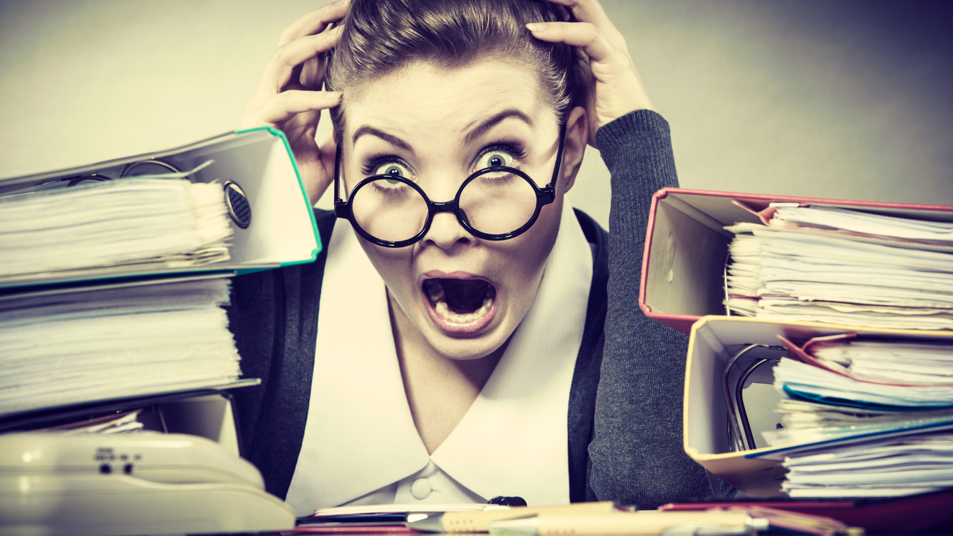 woman in glasses looking scared with piles of files