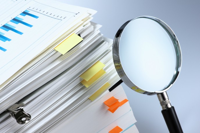 The importance of accurate bookkeeping for audits and investigations - pile of papers with magnifying glass