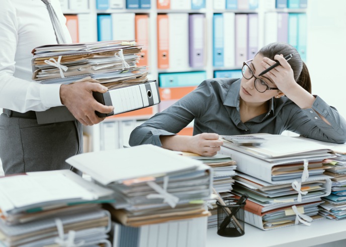 stressed woman with piles of files and being brought more