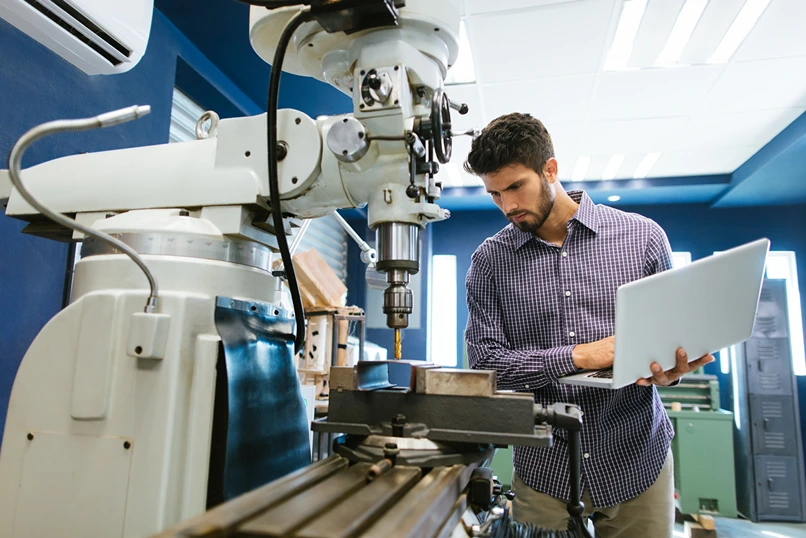 A businessman with a laptop inspecting a drilling machine